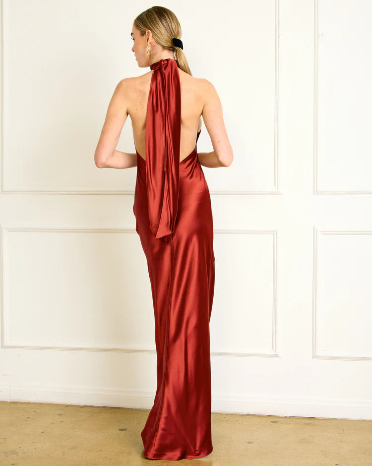 Woman wearing a red satin gown with a halter neck design against a white wall, back view