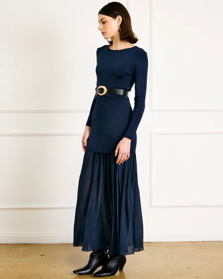 Woman wearing a navy blue dress with a belt against a white wall.