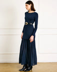 Woman wearing a navy blue dress with a belt against a white wall.