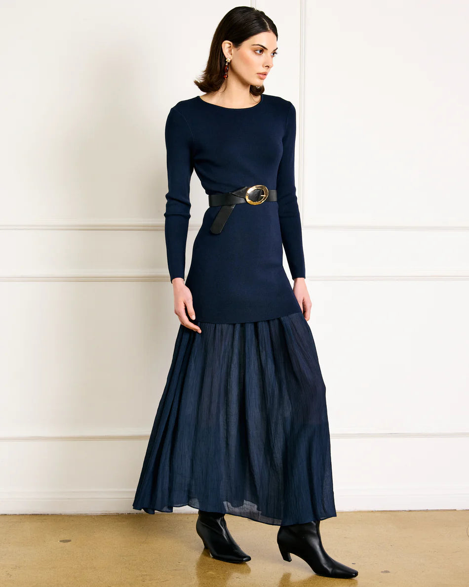 Woman wearing a navy blue dress with a belt against a white wall.