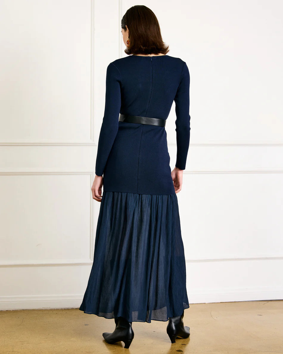 Woman wearing a navy blue dress with a belt against a white wall.