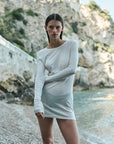 Woman in a white dress standing on a rocky beach with cliffs in the background