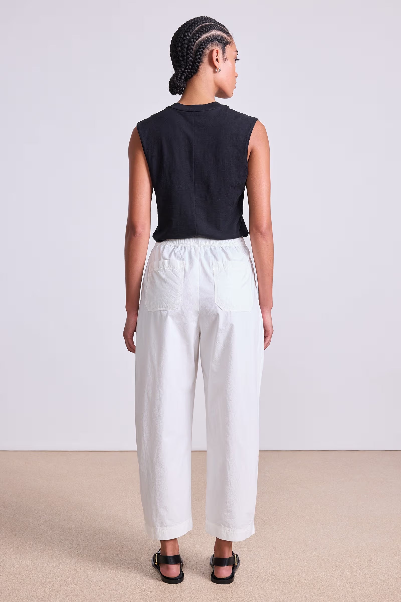 Person wearing a black sleeveless top and white pants on a plain background, back view
