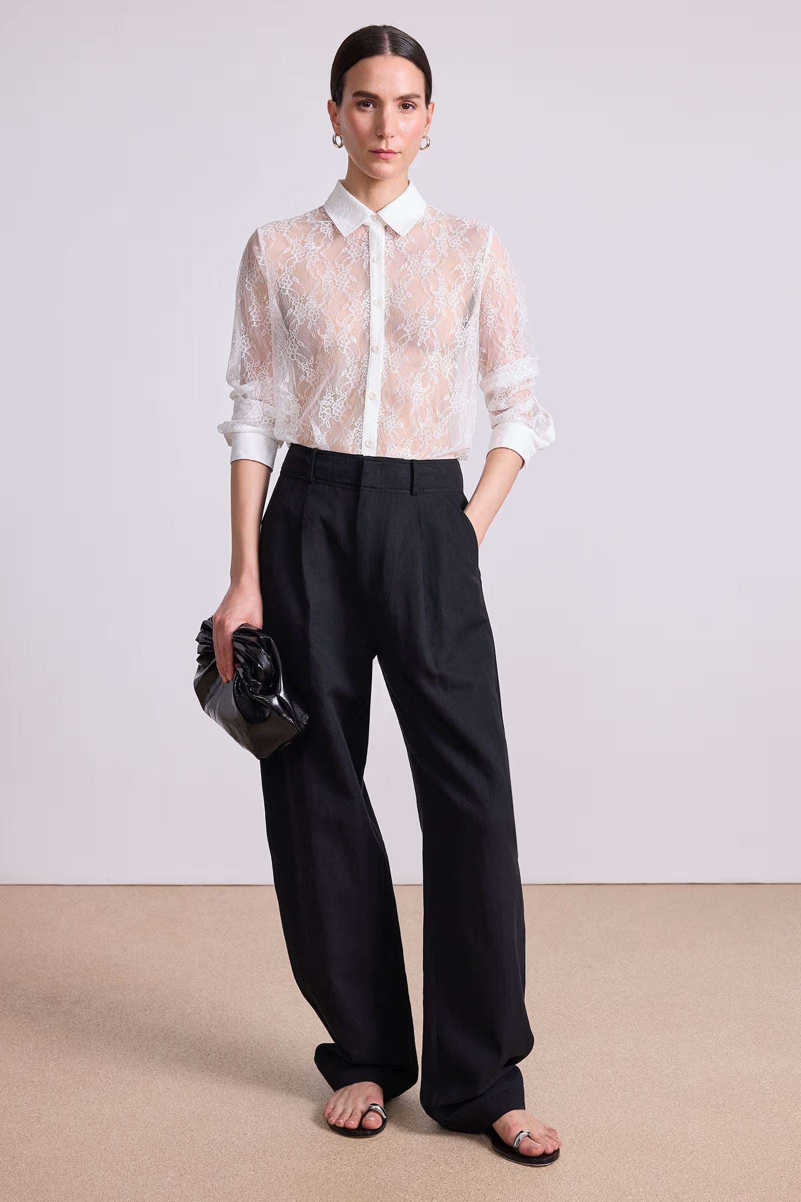 Woman wearing a white lace blouse and black pants on a plain background