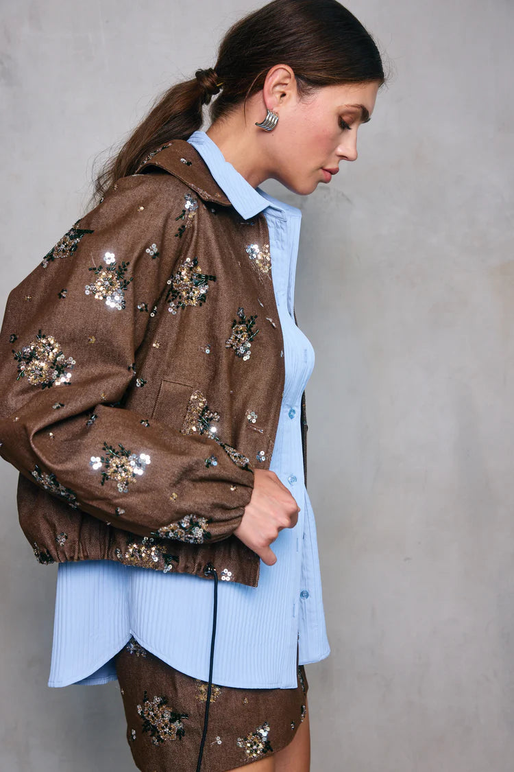 Woman wearing a brown jacket with floral embellishments against a plain background, side view