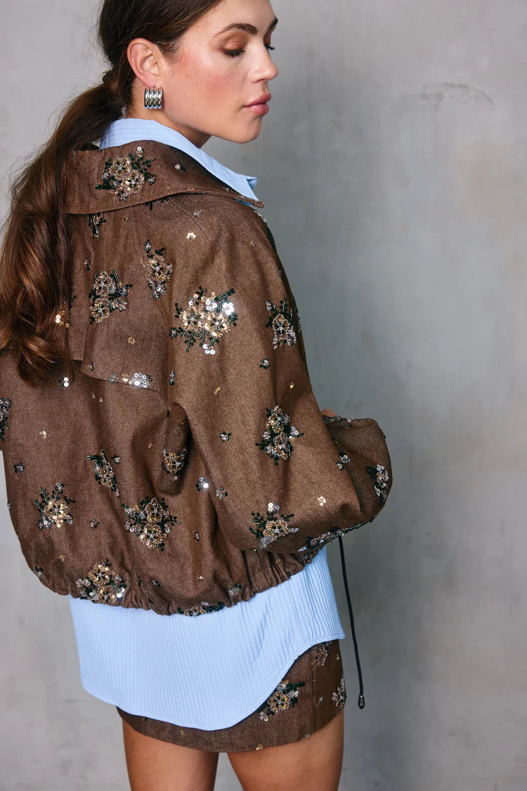 Woman wearing a brown jacket with floral embellishments against a gray background