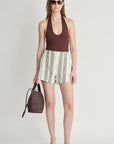 Woman wearing a brown top and striped shorts, holding a woven bag on a white background