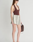 Woman wearing a brown halter top and striped shorts, holding a brown handbag on a white background