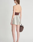 Woman wearing a strapless top and striped skirt with a woven bag on a plain background