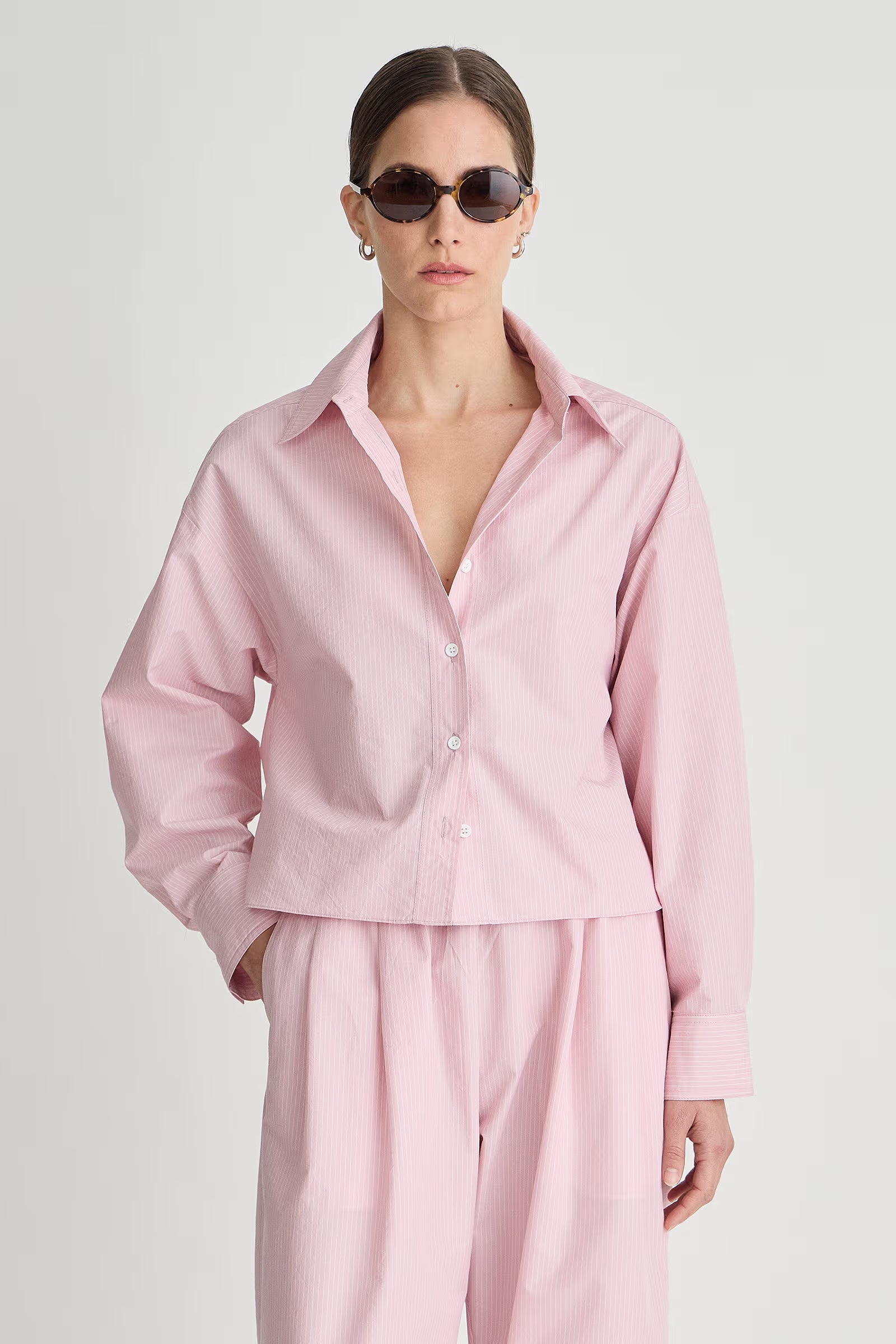 Person wearing a pink outfit with sunglasses on a light gray background