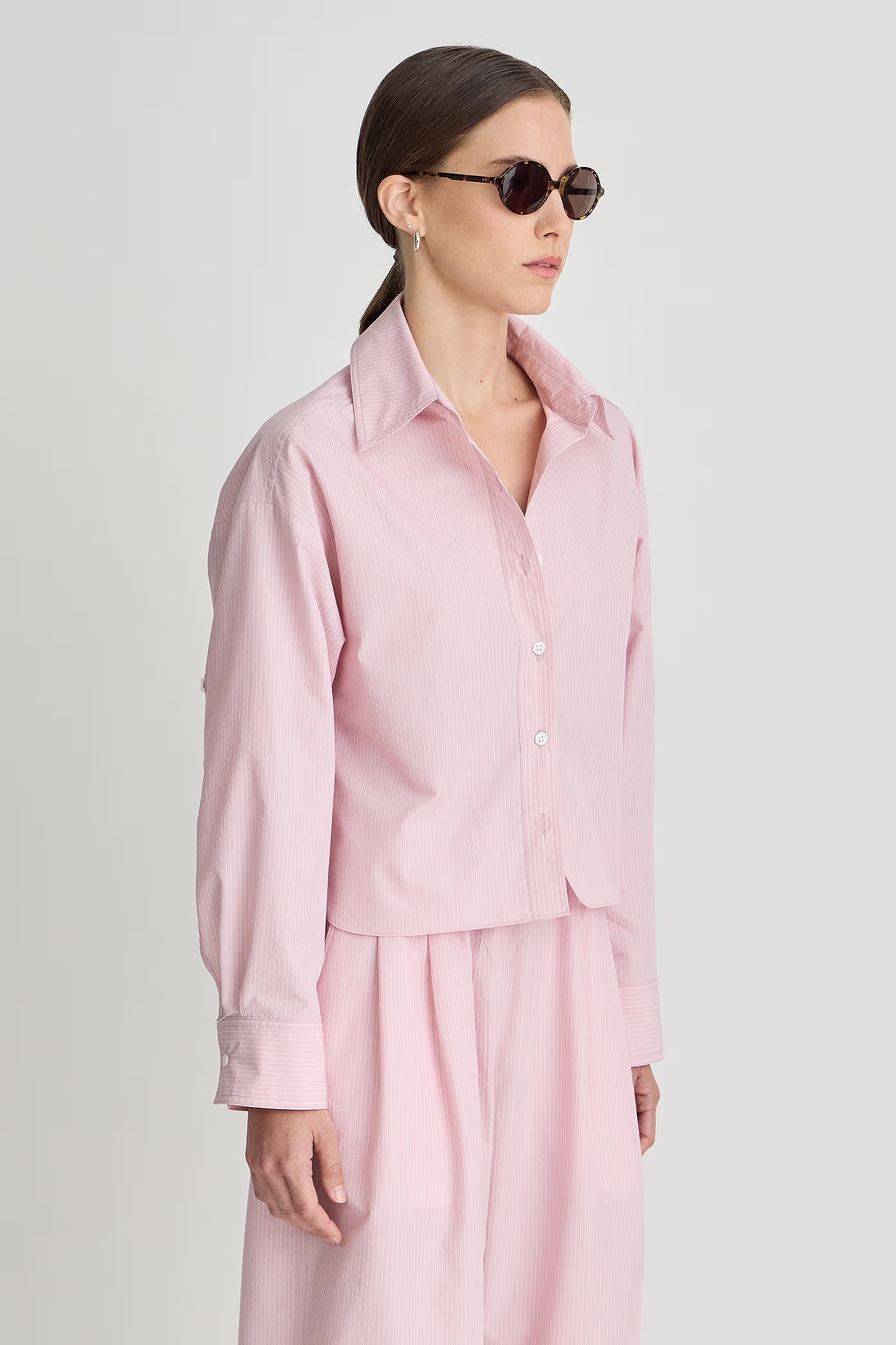 Woman wearing a pink outfit with sunglasses on a plain background