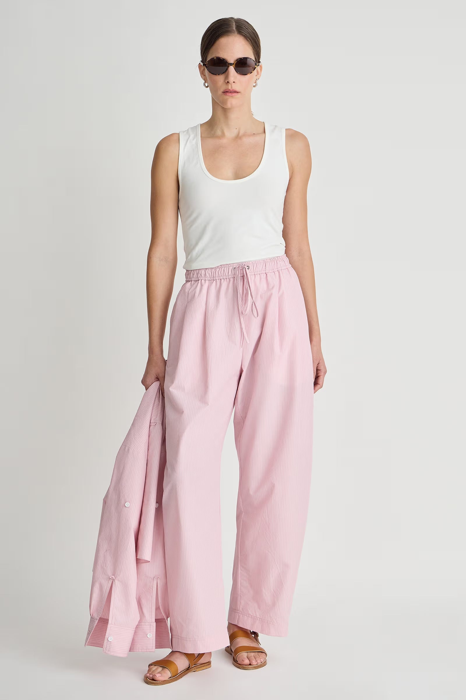 Woman wearing a white tank top and pink pants on a plain background