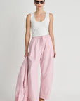 Woman wearing a white tank top and pink pants on a plain background