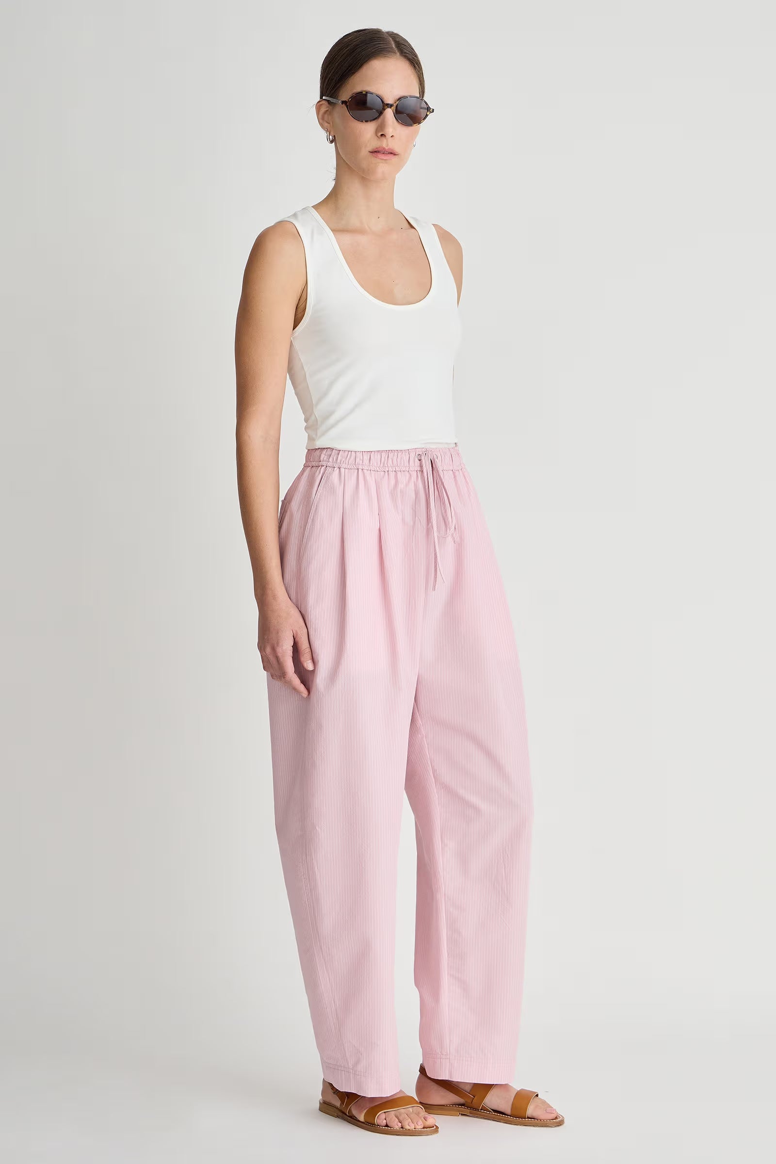 Woman wearing a white tank top and pink pants on a plain background