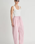 Woman wearing a white tank top and pink pants on a plain background