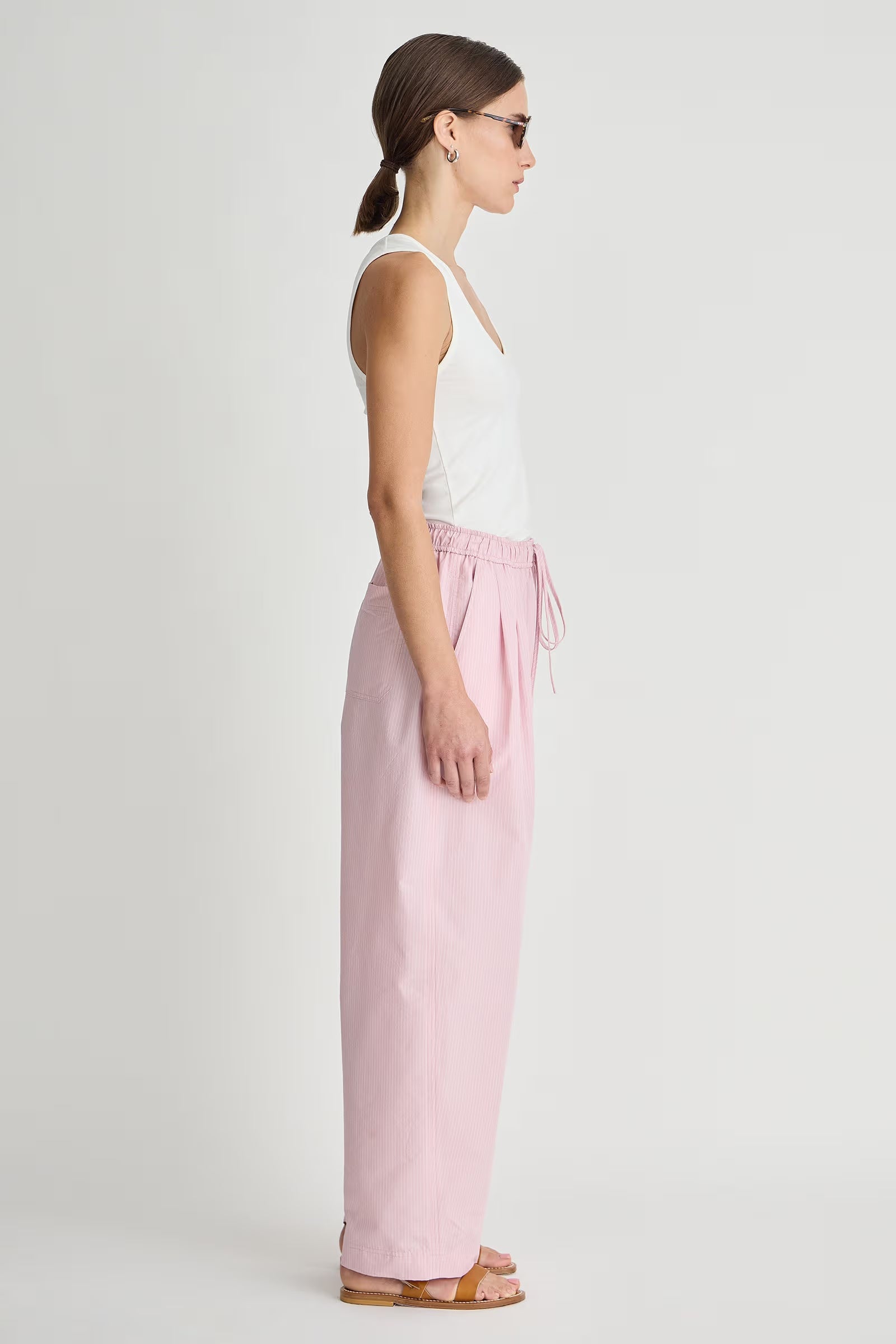 Woman wearing a white tank top and pink pants on a white background