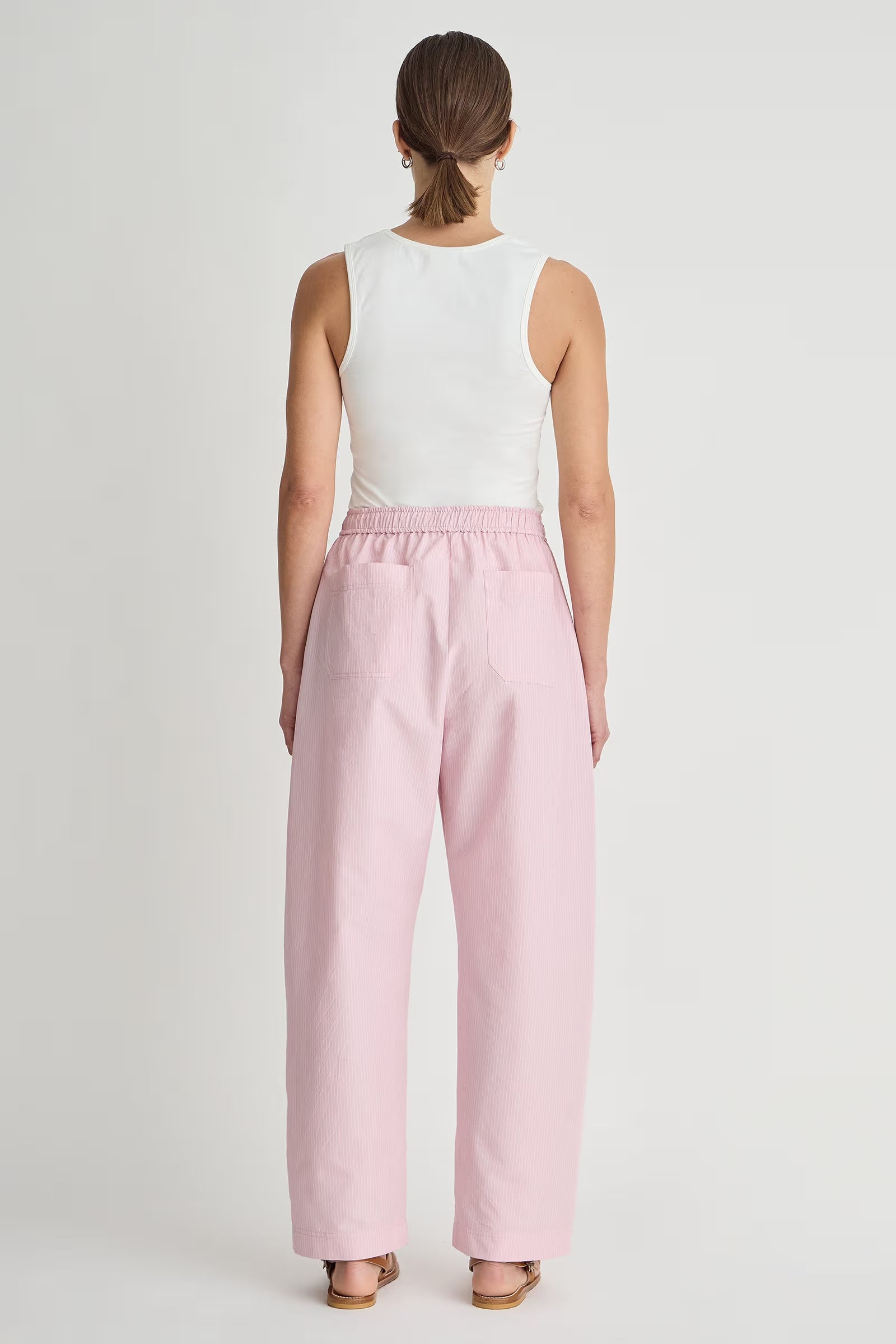 Person wearing a white sleeveless top and pink pants on a light gray background