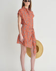 Woman wearing an orange patterned dress with a straw hat on a white background
