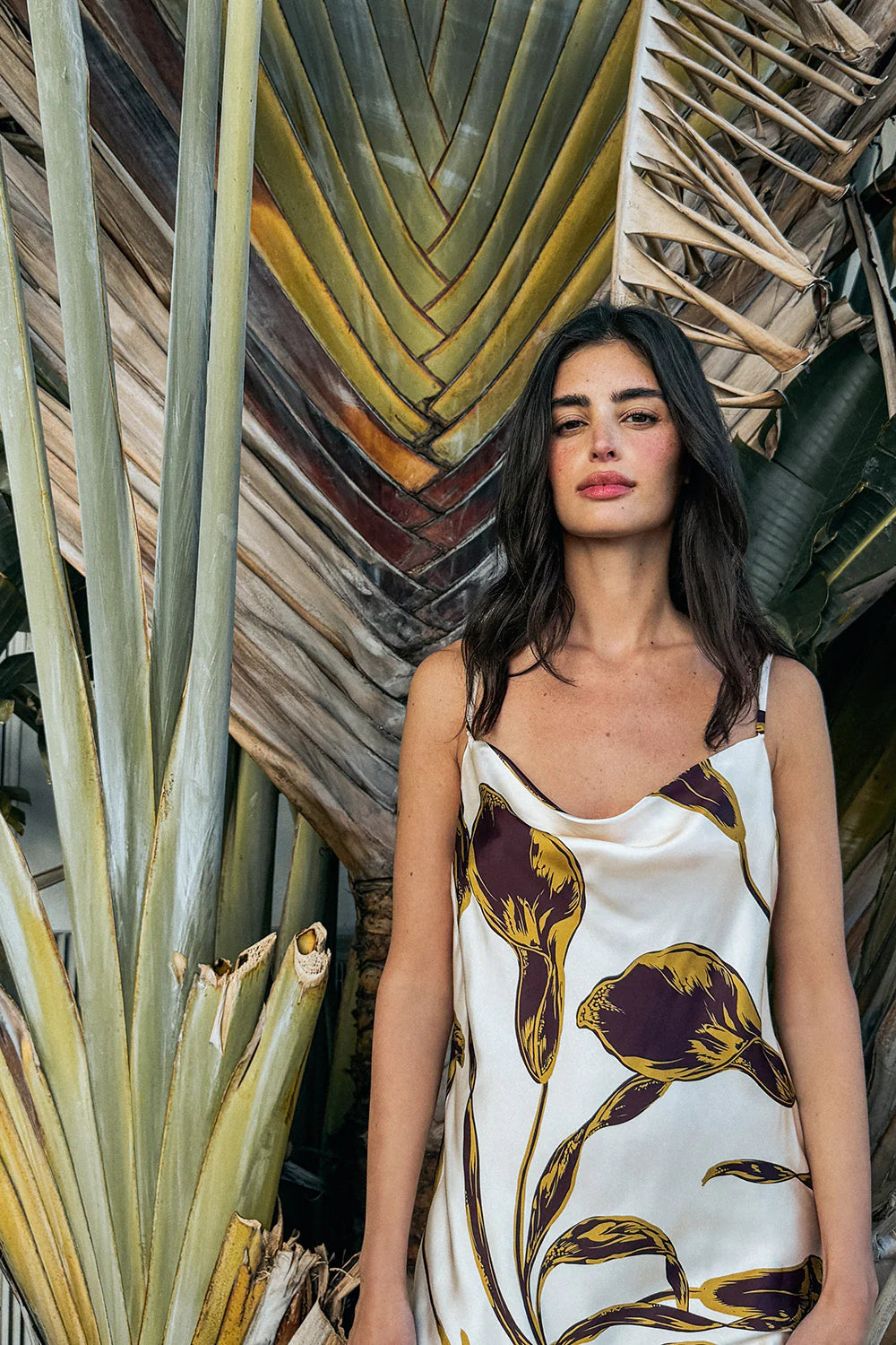 Woman wearing Mia Dress standing among plants with a textured wall in the background