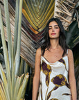 Woman wearing Mia Dress standing among plants with a textured wall in the background
