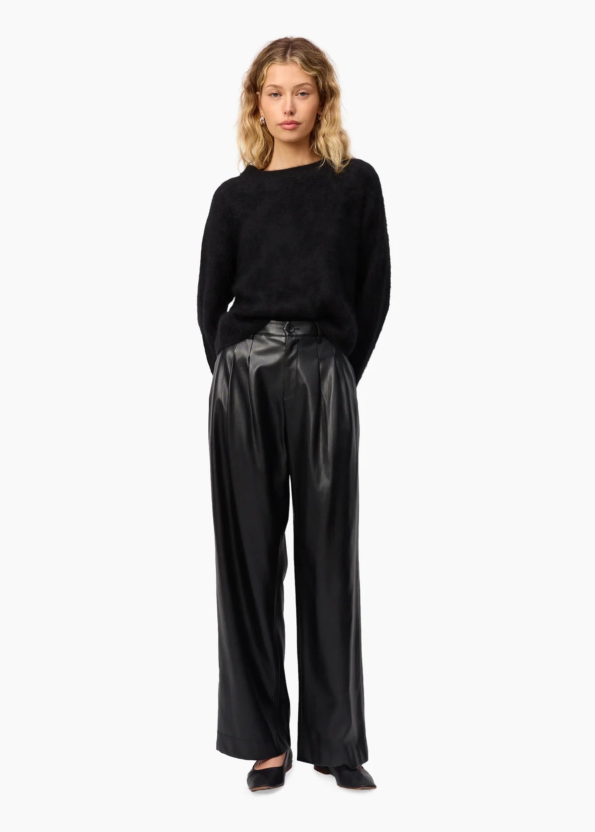 Woman wearing a black sweater and shiny black pants on a white background, front view