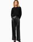 Woman wearing a black sweater and shiny black pants on a white background, front view