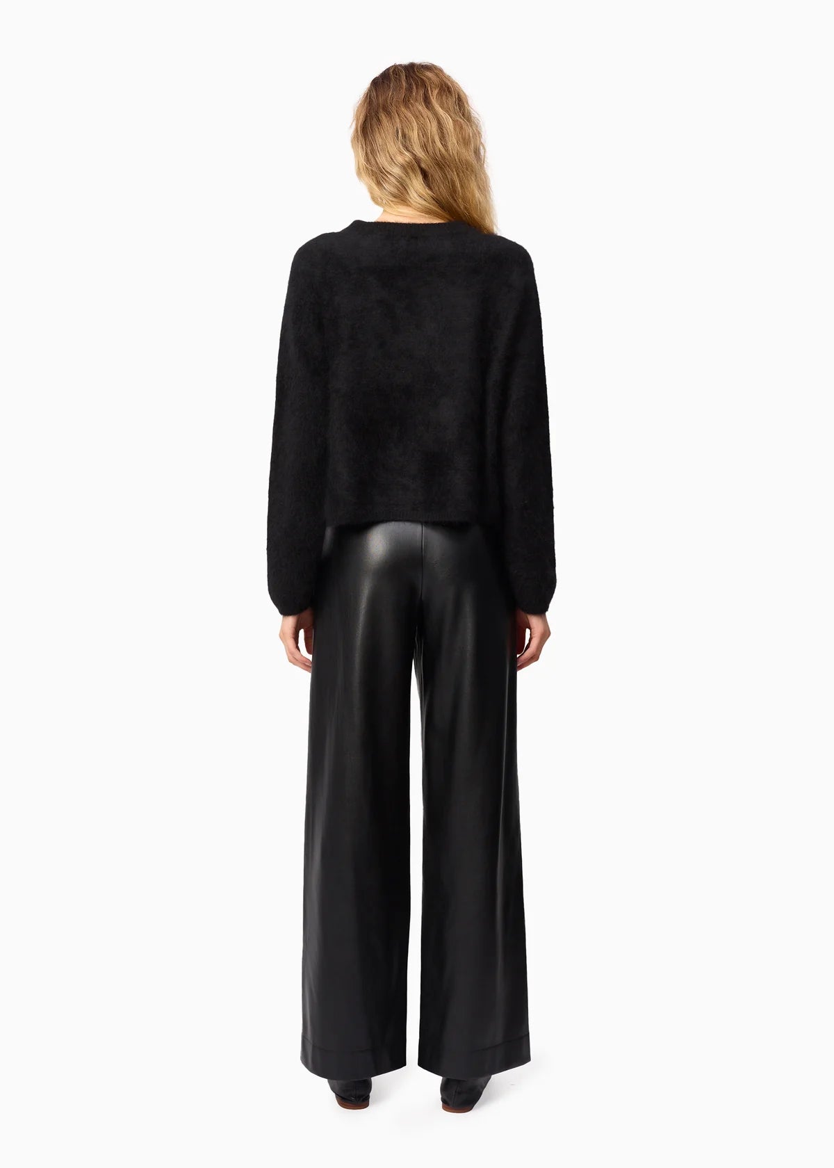 Person wearing a black sweater and black leather pants on a white background, back view
