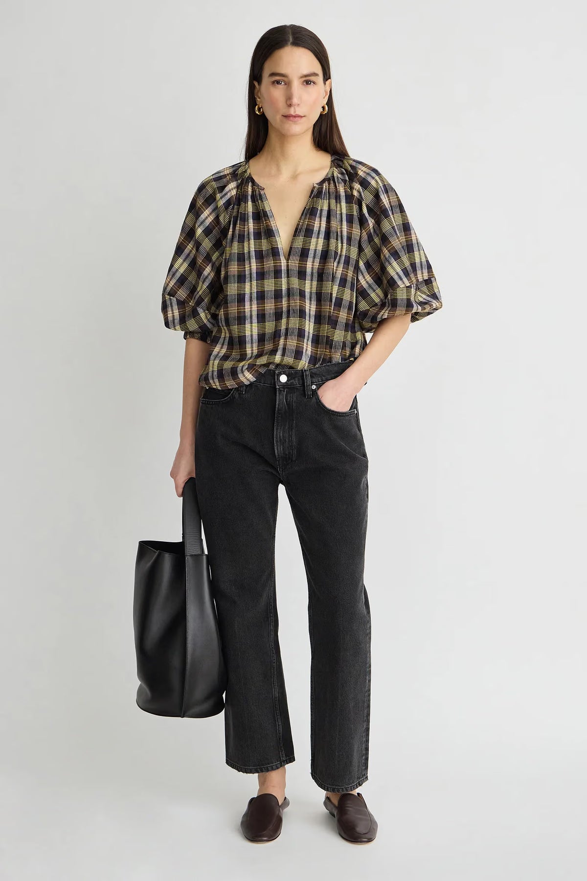 model wearing a plaid vneck short sleeve top with black jeans carrying a black bag on a grey background 