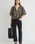 model wearing a plaid vneck short sleeve top with black jeans carrying a black bag on a grey background 