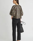 model wearing a plaid vneck short sleeve top with black jeans carrying a black bag on a grey background, back view 