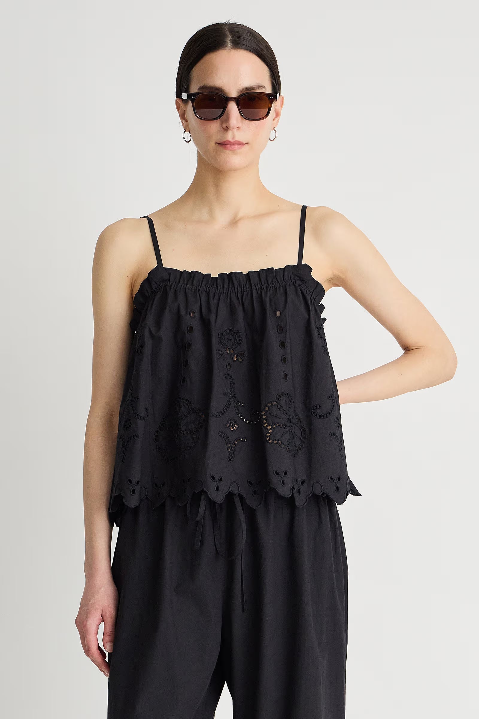 Woman wearing a black sleeveless top with intricate detailing on a plain background