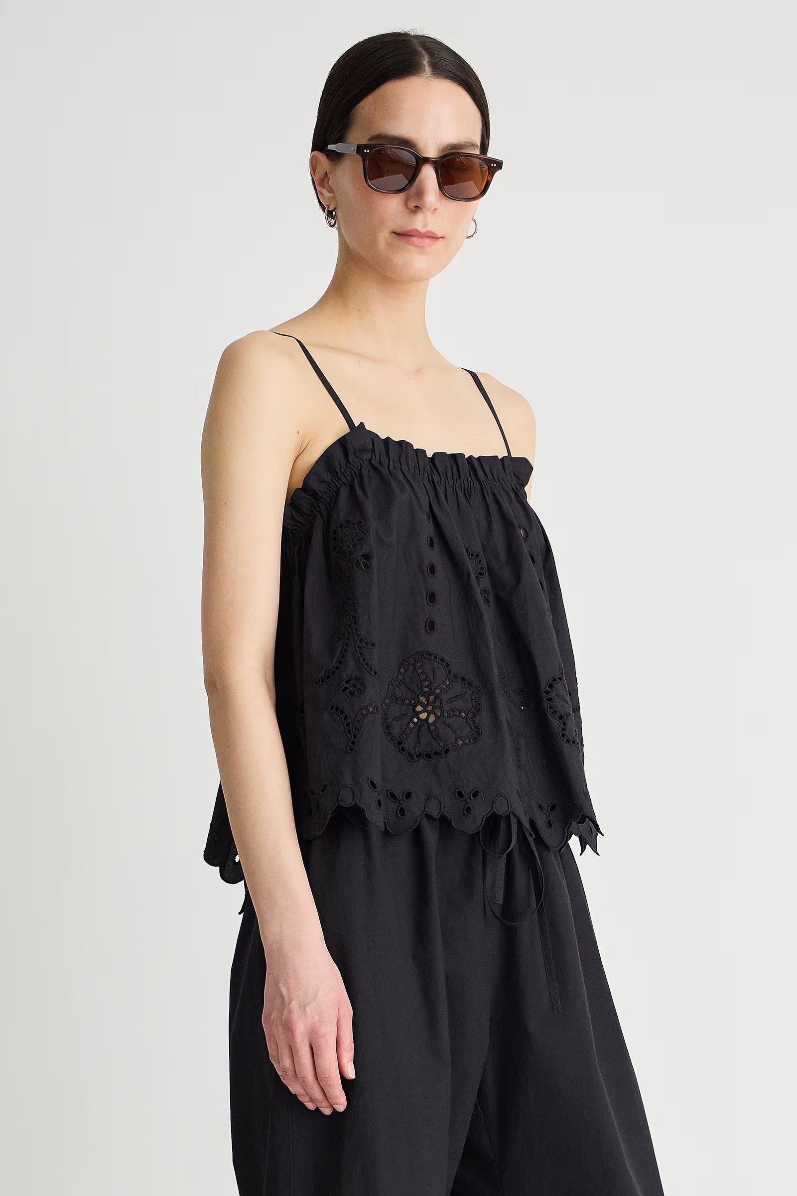 Woman wearing a black sleeveless top with floral embroidery on a plain background