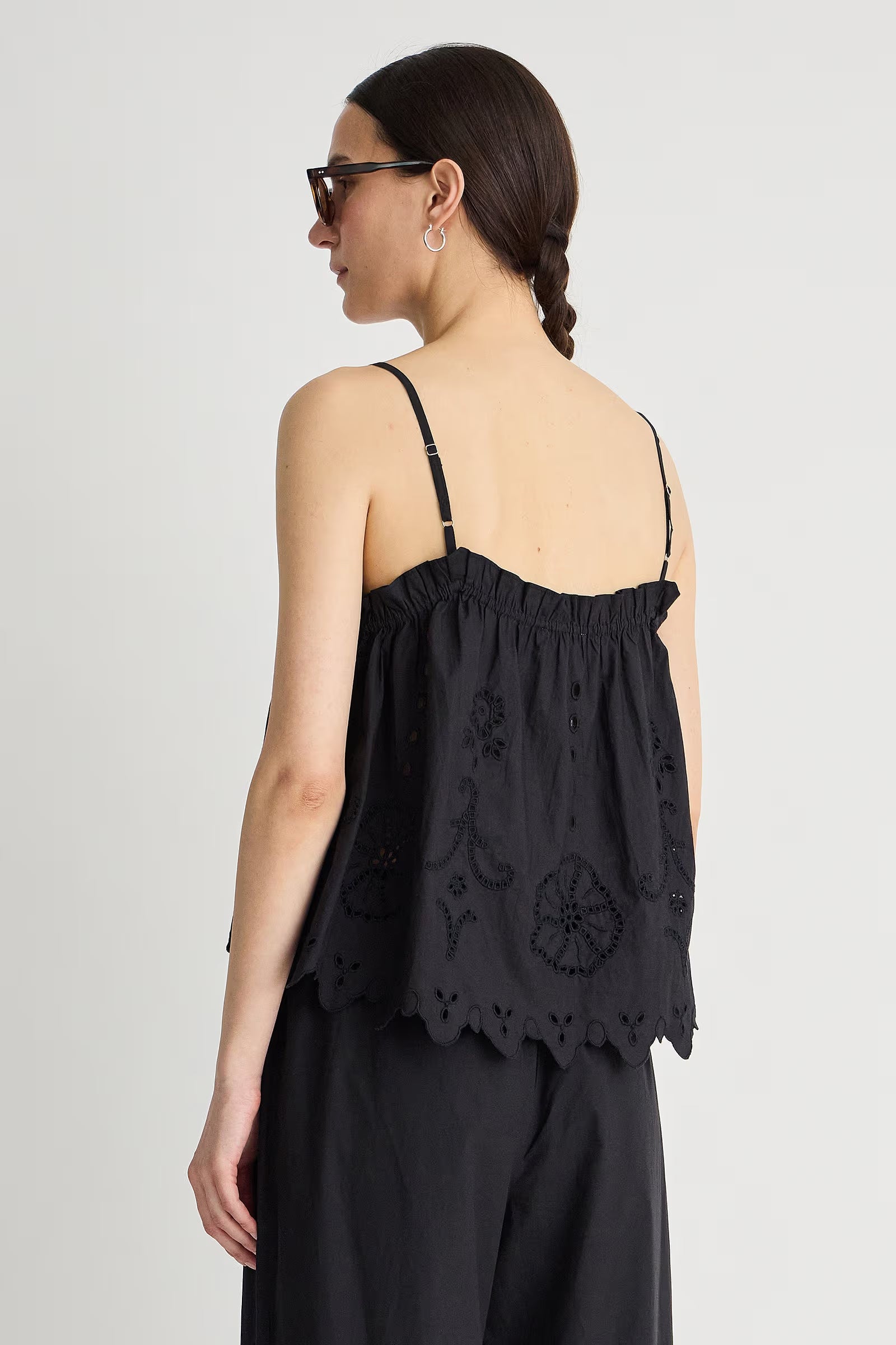 Woman wearing a black sleeveless top with intricate designs on a plain background