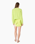 A woman shown from the back wearing a bright neon yellow-green ribbed knit cardigan and matching mini skirt against a plain white background.