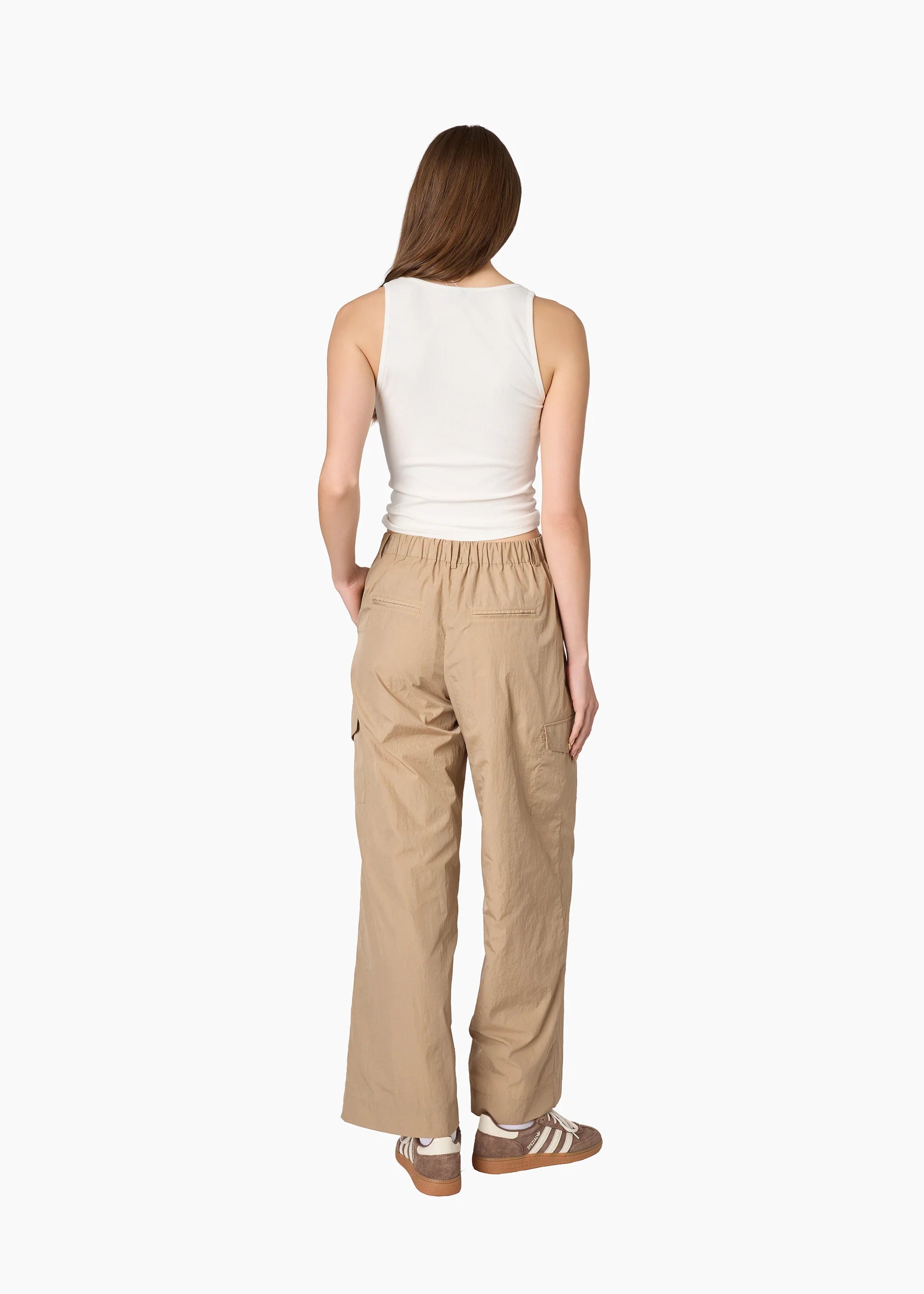 A woman shown from the back wearing beige wide-leg cargo pants, a white sleeveless top, and brown sneakers against a plain white background. 