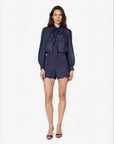 model wearing a navy sheer top with a tie neck with navy shorts that lace a small lace trim on a white background 