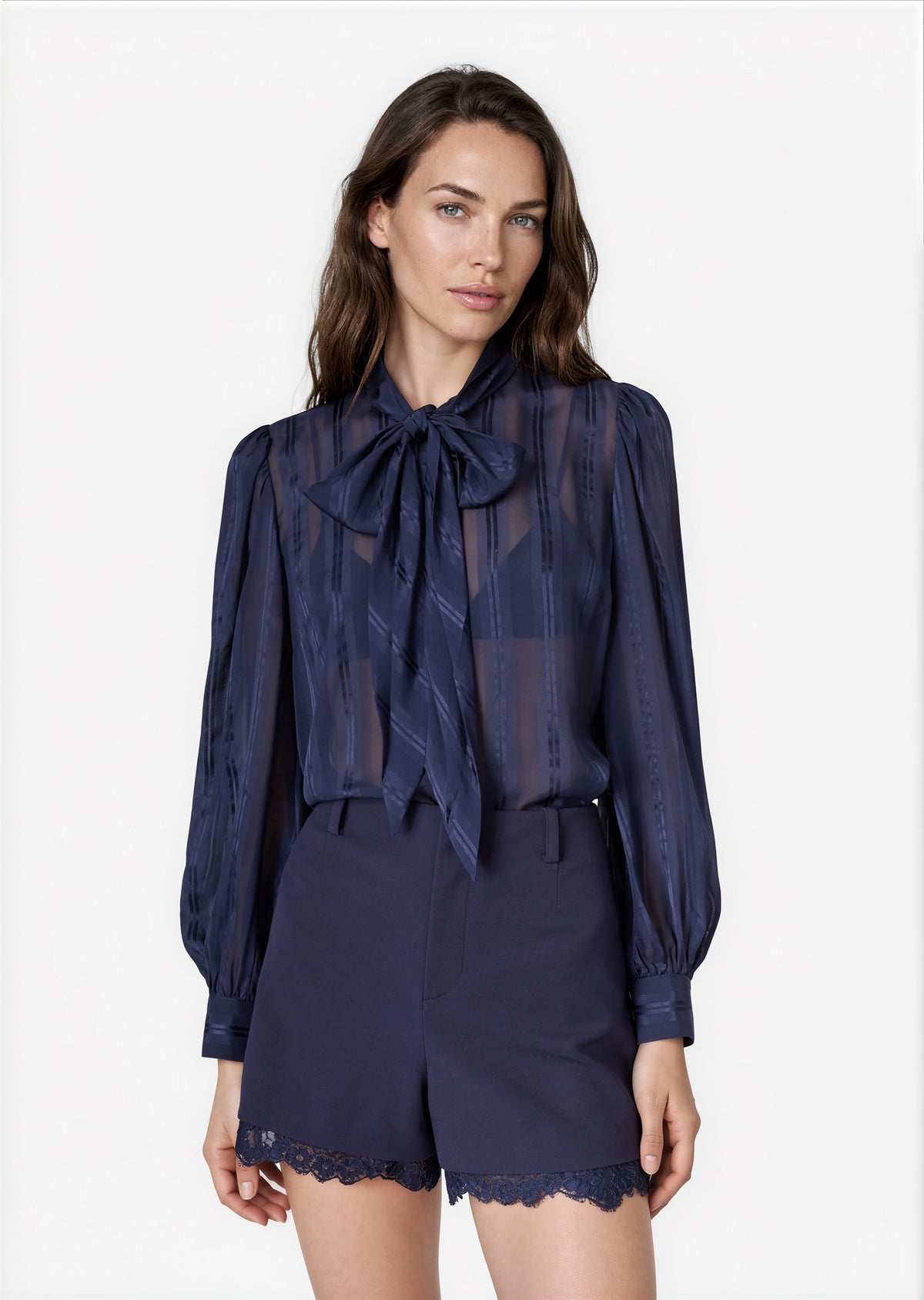 model wearing a navy sheer top with a tie neck with navy shorts that lace a small lace trim on a white background 