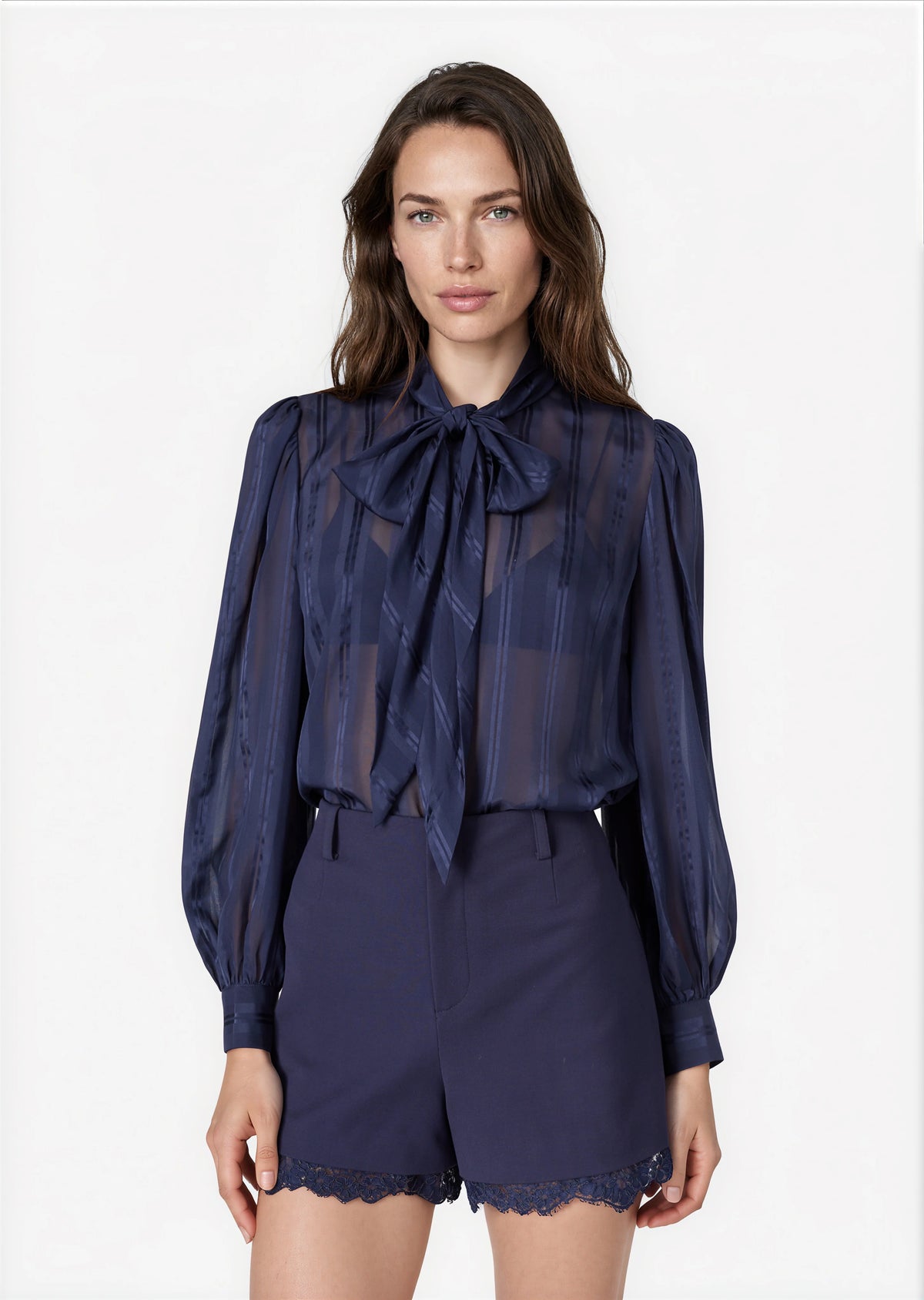 model wearing a navy sheer top with a tie neck with navy shorts that lace a small lace trim on a white background 