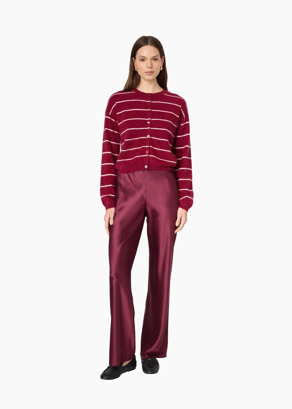 A woman modeling a burgundy cardigan with thin white horizontal stripes and matching satin trousers against a plain white background.
