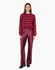 A woman modeling a burgundy cardigan with thin white horizontal stripes and matching satin trousers against a plain white background.
