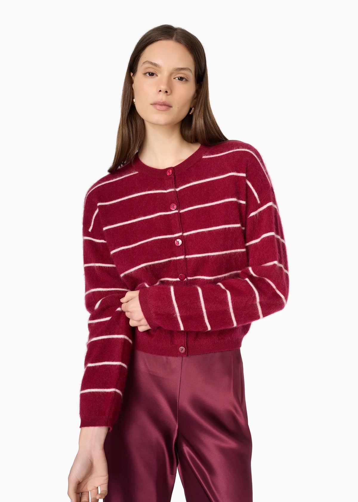 A woman wearing a burgundy cardigan with thin white horizontal stripes and matching satin trousers, photographed against a clean white studio background.