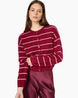 A woman wearing a burgundy cardigan with thin white horizontal stripes and matching satin trousers, photographed against a clean white studio background.