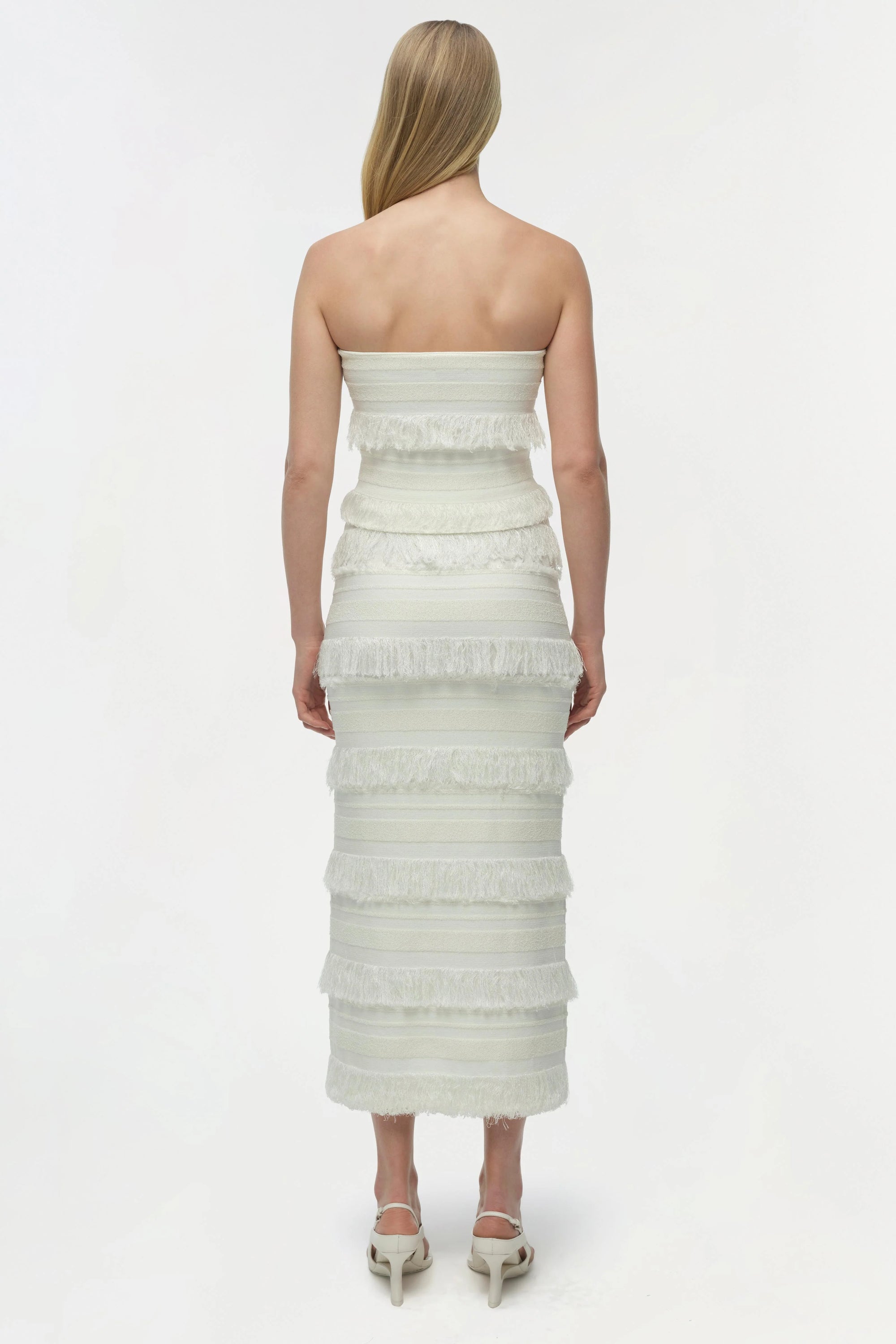 Woman wearing a strapless, tiered white dress on a plain background