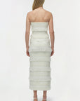 Woman wearing a strapless, tiered white dress on a plain background