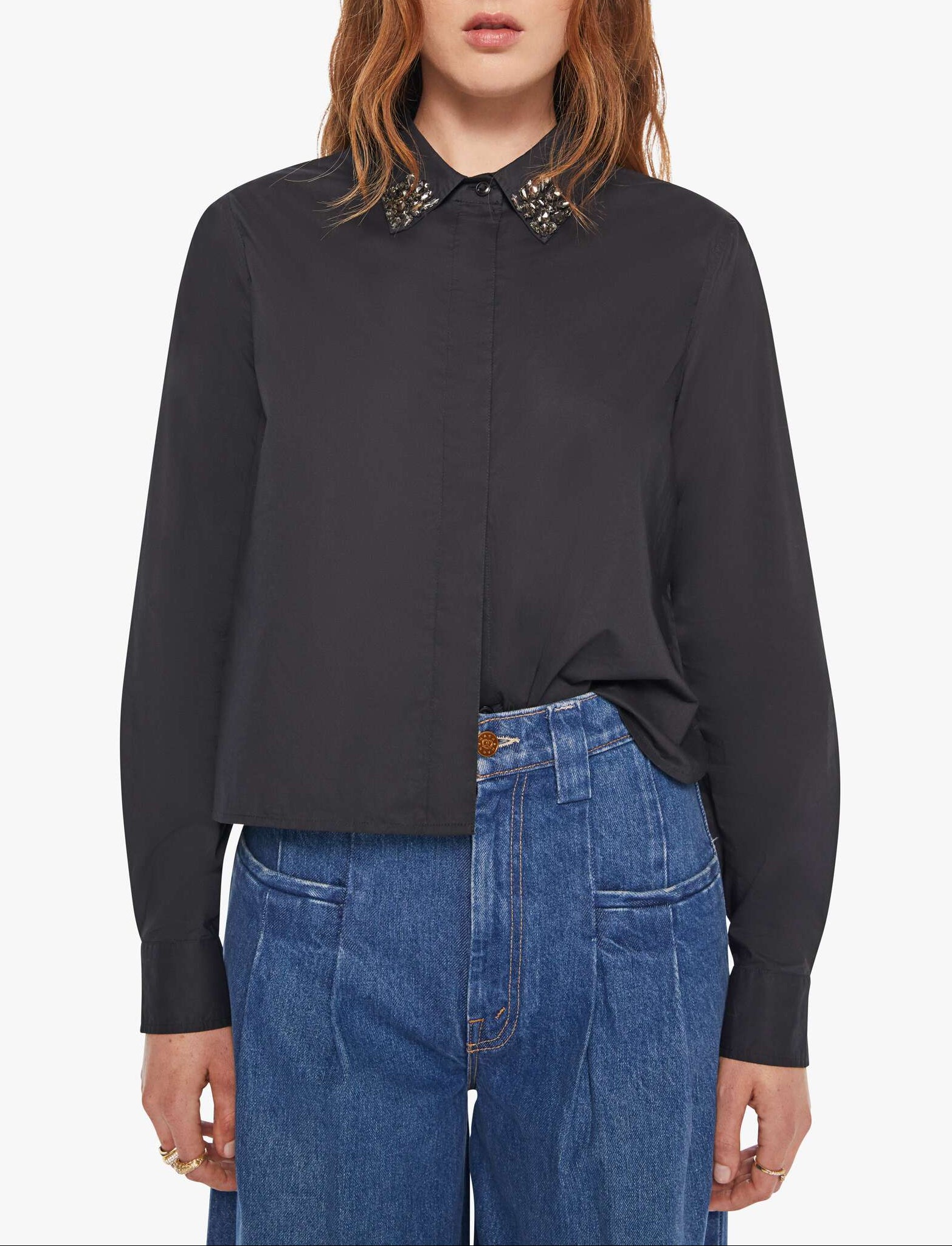 Person wearing a black shirt with a decorative collar and blue jeans on a white background