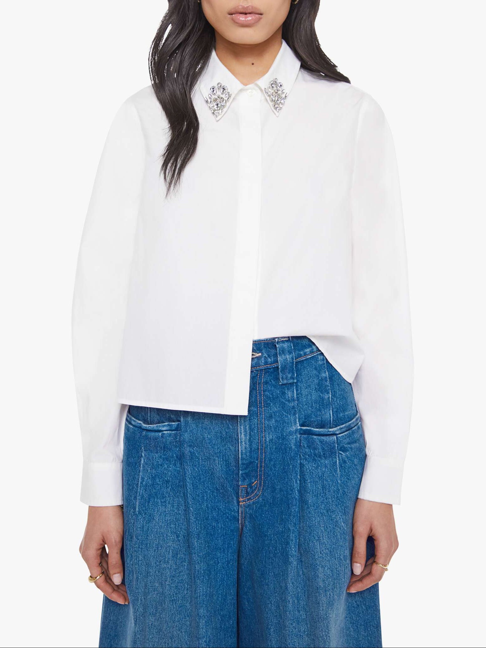 Woman wearing a white blouse with embellishments and blue jeans on a white background