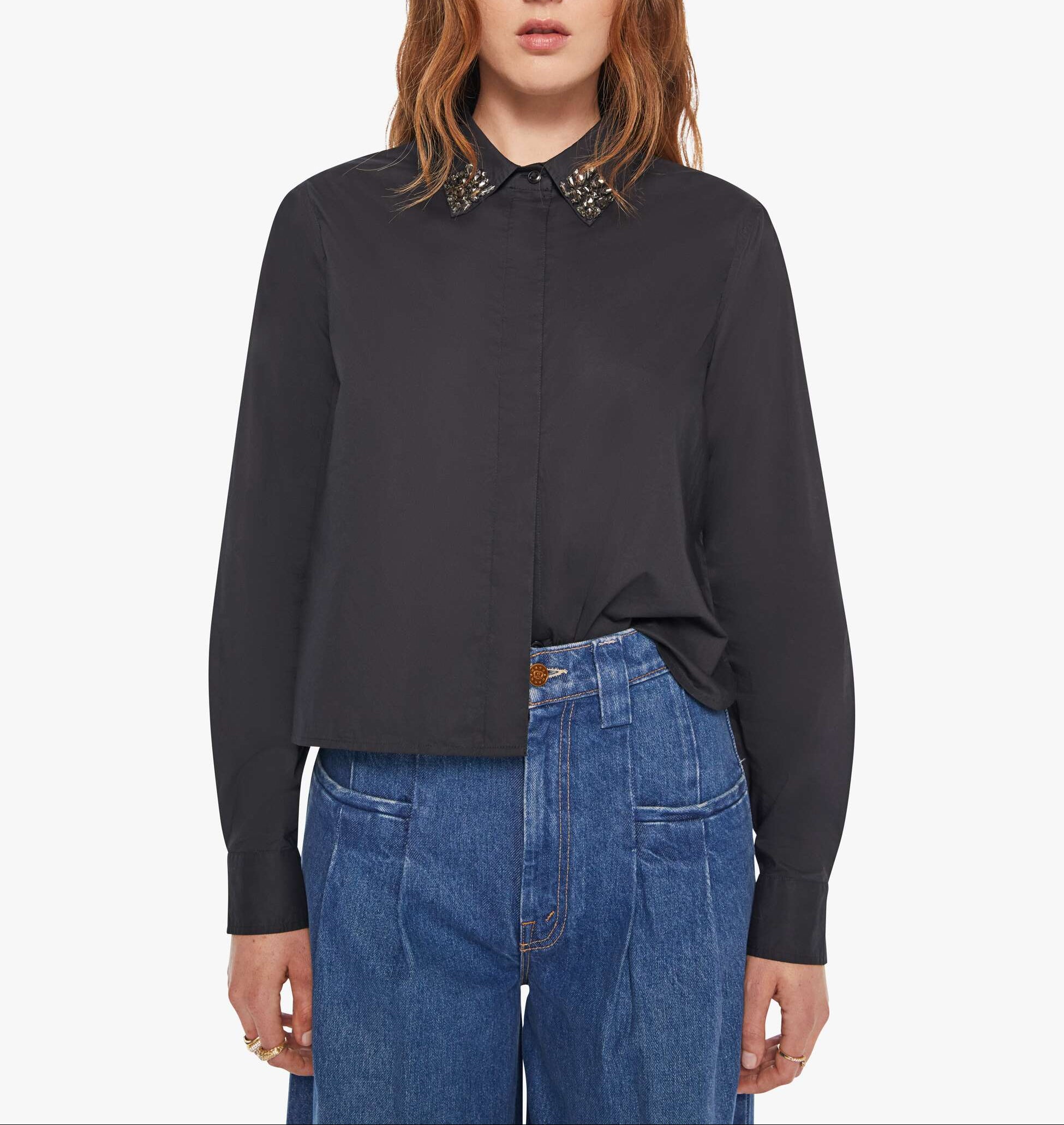 Person wearing a black shirt with a decorative collar and blue jeans on a white background