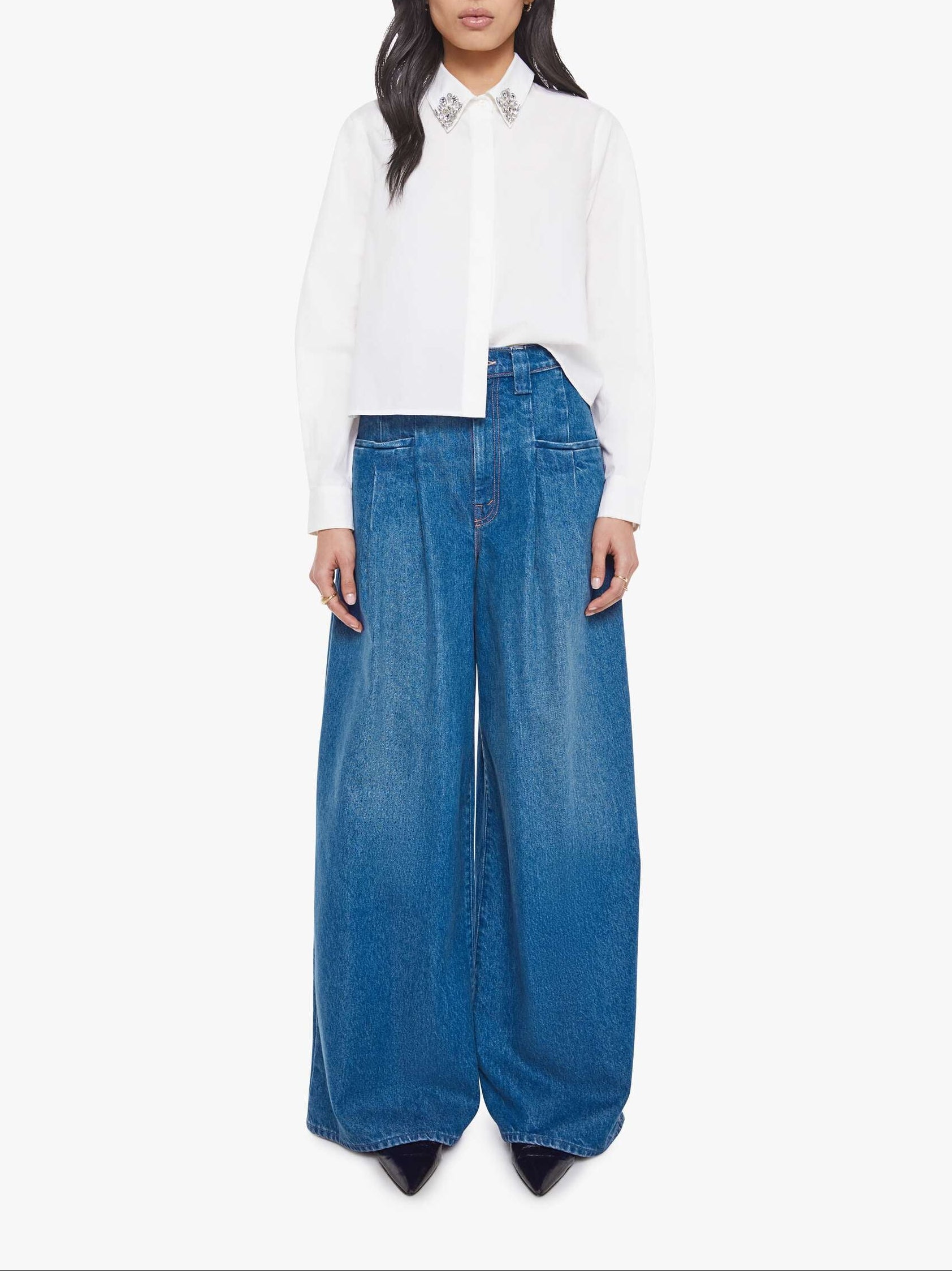 Woman wearing a white blouse and blue wide-leg jeans on a white background