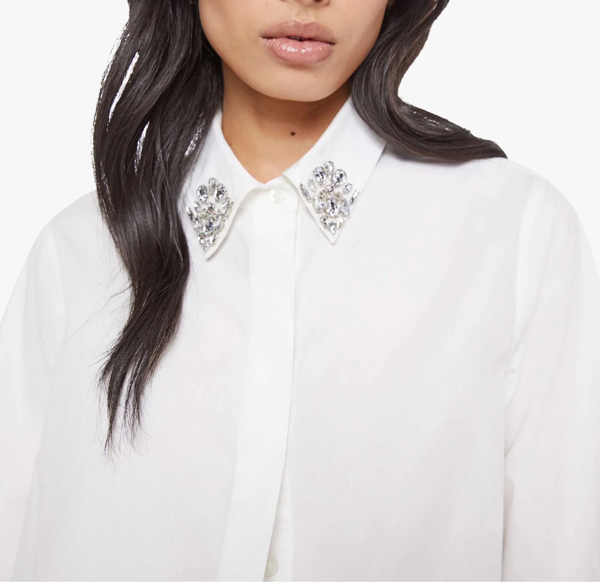 Woman wearing a white blouse with embellished collar against a plain background
