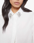 Woman wearing a white blouse with embellished collar against a plain background